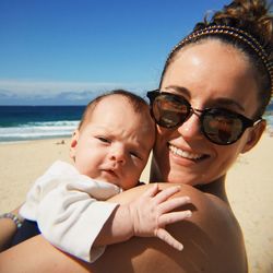 Portrait of mother holding cute baby at beach against sky