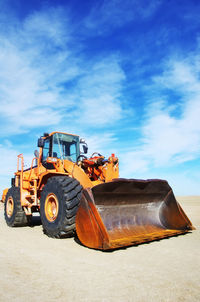 Bulldozer on field against cloudy blue sky