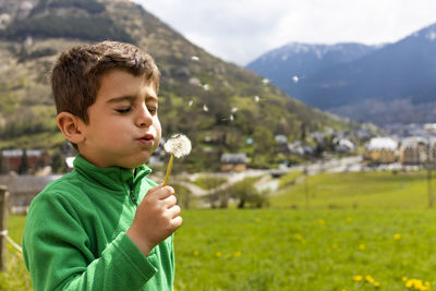 Cute boy blowing dandelion on field