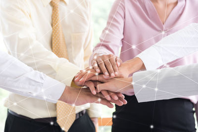 Digital composite image of colleagues stacking hands at office