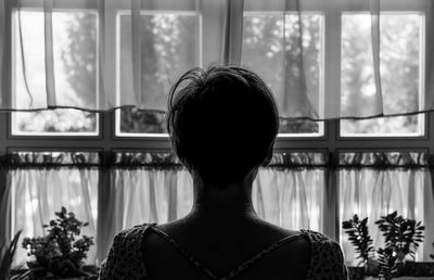 Rear view of woman standing by window at home
