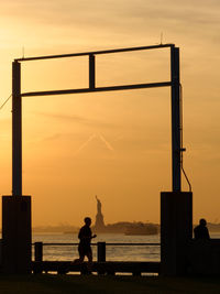 Silhouette men by river against orange sky