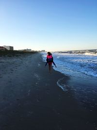 Man walking on beach against clear sky