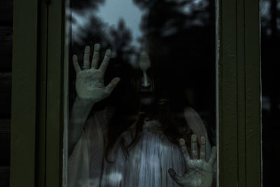 Spooky ghost looking through glass window of haunted cabin