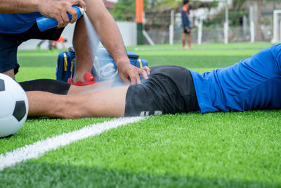 Low section of male physical therapist spraying on soccer player leg at field