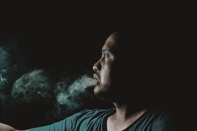 Mid adult man emitting smoke against black background