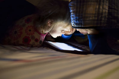 Siblings using tablet computer on bed in darkroom at home