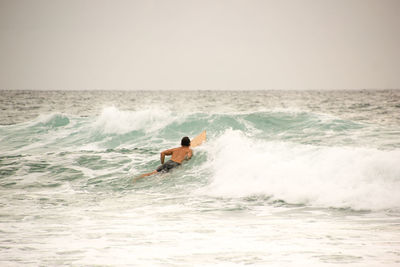 Rear view of shirtless man surfing in sea against sky