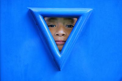 Close-up portrait of cute boy peeking through hole in blue wall