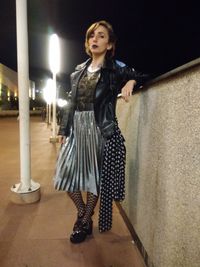 Portrait of young woman standing against illuminated wall