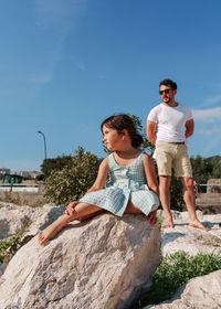 Side view of girl sitting on rock with father on background 
