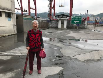 Full length senior woman standing on street during rainy season