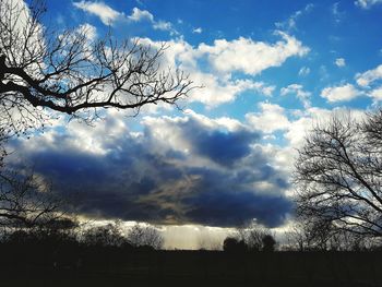 Low angle view of bare trees against cloudy sky