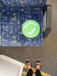 Low section of woman looking down at safety sign on seat in public transport