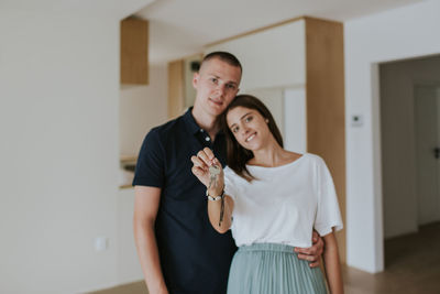 Portrait of smiling young couple with house key standing at home