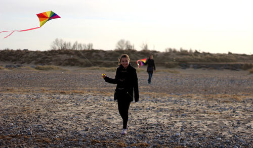 Girl holding kite with mother on field against sky