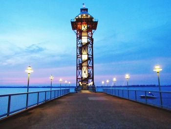 Illuminated lighthouse by sea against sky at dusk