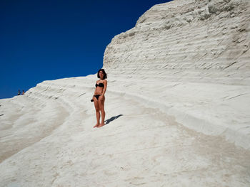 Full length of young woman in bikini standing on sand dune