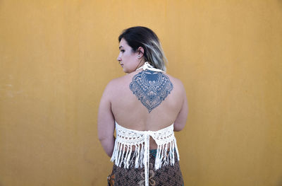 Rear view of young girl showing her tattoo in back against yellow wall