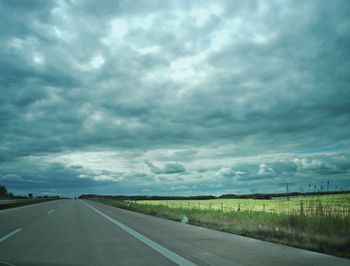 Road passing through field against cloudy sky