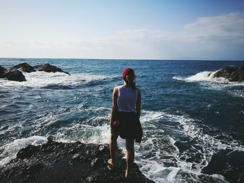 Rear view of woman standing on rock by sea