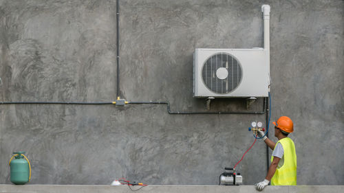 Manual worker repairing air conditioner against wall