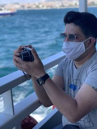 Young man photographing with camera on sea by railing