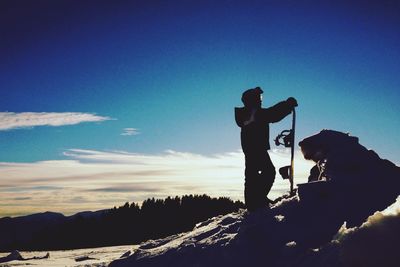 Silhouette of people standing on mountain against sky at sunset