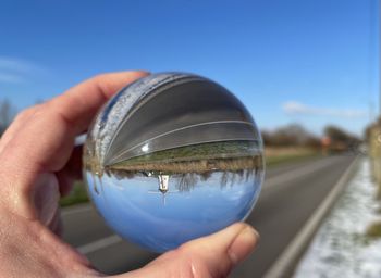 Cropped image of hand holding crystal ball against clear sky