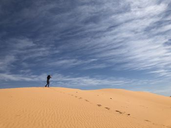 Rear view of man walking on sand dune in desert against cloudy sky