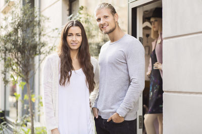 Portrait of smiling owner with female worker standing outside clothing store