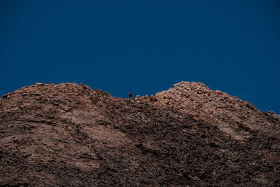 Low angle view of man on rock against blue sky