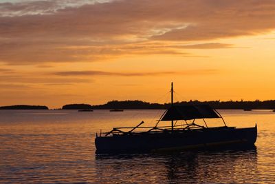 Silhouette sailboat in sea against sky during sunset