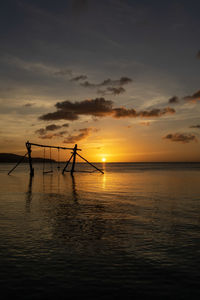 Silhouette wooden posts in sea against sky during sunset