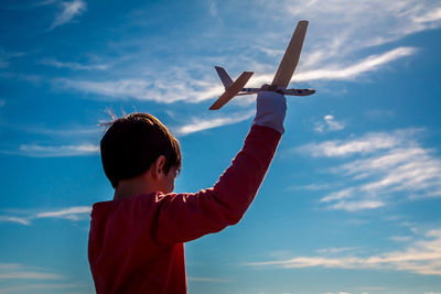 Low angle view of boy holding airplane model against blue sky