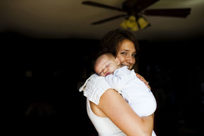 Portrait of smiling mother carrying baby girl at home