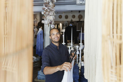 Smiling male owner holding coathanger while standing at fashion store