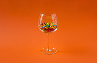 Colorful candies in a wine glass on the orange colored background, minimalism