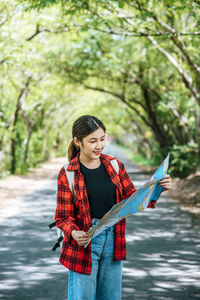 Young woman with arms raised standing against trees