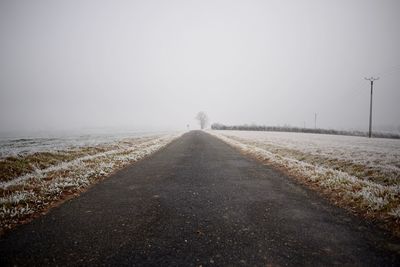 Road on field against clear sky during winter