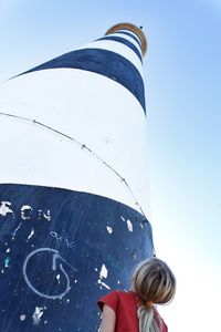 Low angle view of girl standing by lighthouse against sky