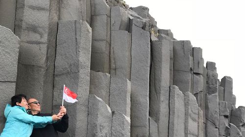 People holding singaporean flag against stone wall