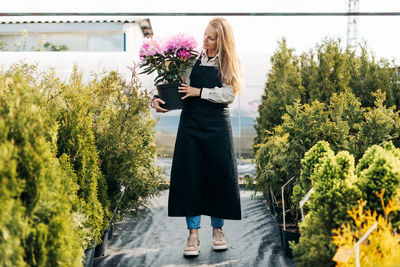 A girl gardener with a beautiful flowering rhododendron in her hands checks coniferous 