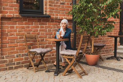 Portrait of man sitting on chair against brick wall
