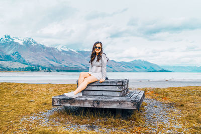 Portrait of young woman sitting on mountain against sky