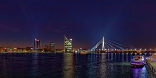 Illuminated city by river against sky at night