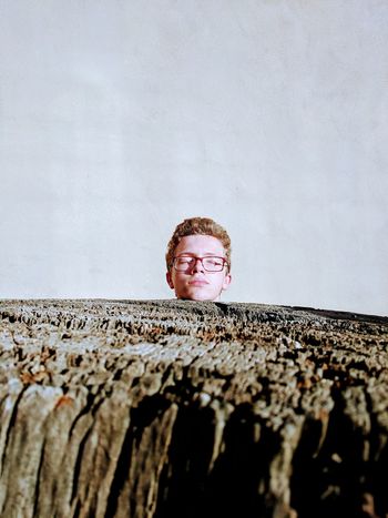 Teenage boy with eyes closed standing by wood against wall