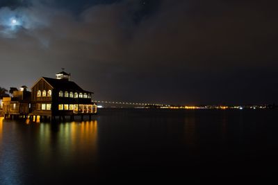 Illuminated building by sea against sky at night