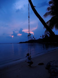 High angle view of woman using phone while sitting on swing at beach at dusk