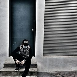 Man wearing surgical mask sitting on steps at entrance of building